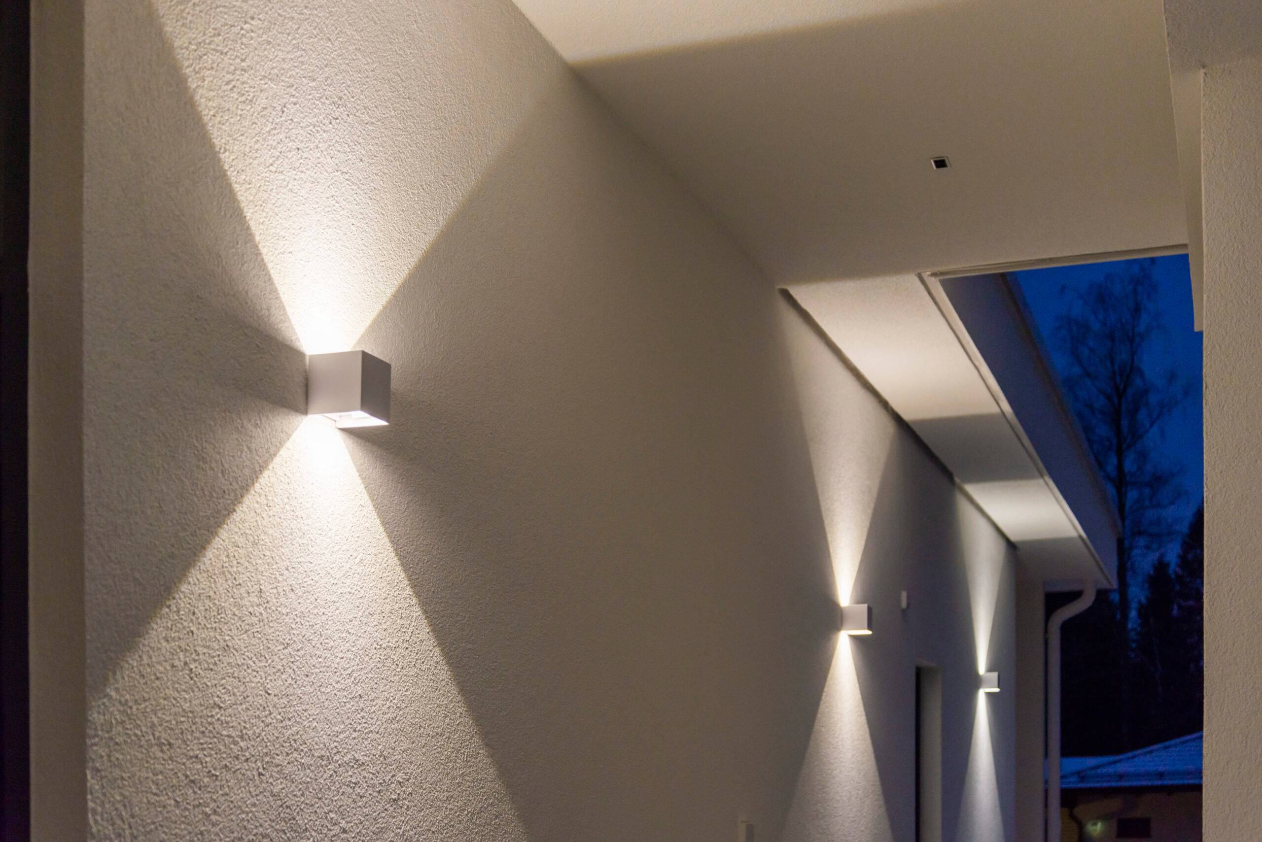 Le luci LED cubiche bianche da parete illuminano sia verso l'alto che verso il basso, creando un disegno netto di luce sulla parete.