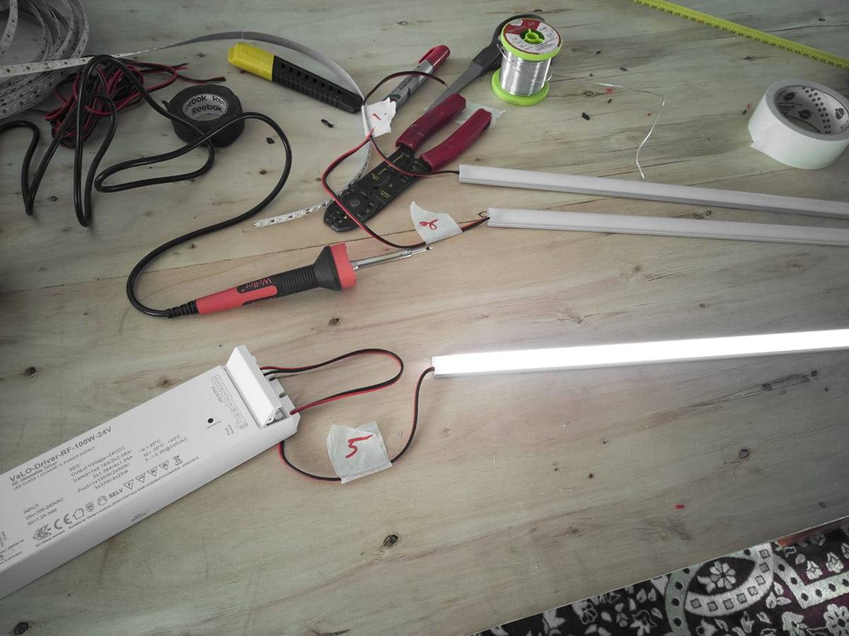 Banco da lavoro con utensili elettrici, strisce LED, fili, tubi fluorescenti incandescenti; include pinze, multimetro, filo per saldare e alimentatore.