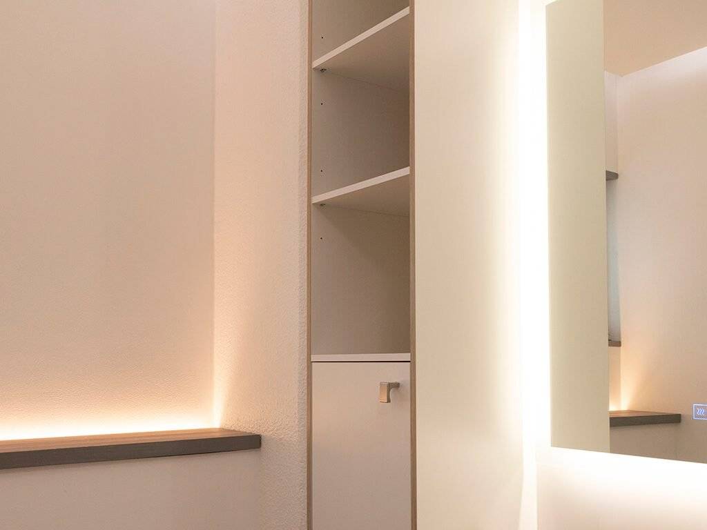 Arredamento minimalista, moderni scaffali illuminati a LED, parete a specchio, illuminazione soffusa. I colori neutri e le linee pulite creano uno spazio elegante e raffinato.