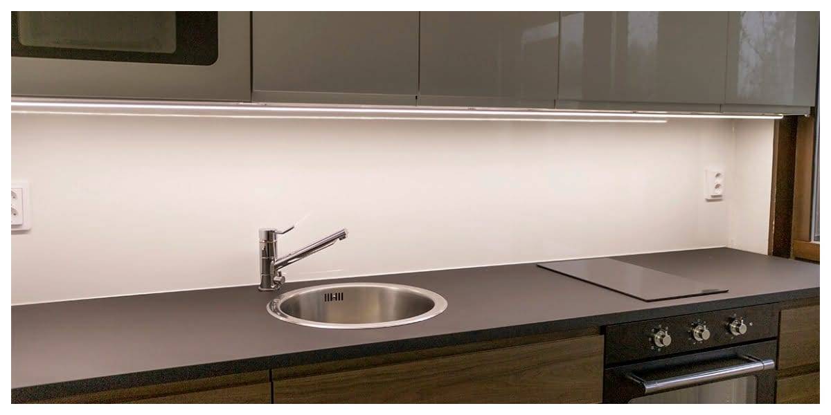 L'illuminazione in cucina - l'illuminazione giusta per le attività della cucina Cucina moderna con illuminazione LED del mobile, elegante piano di lavoro scuro, lavello in acciaio inox, rubinetto monocomando, piano cottura illuminato e armadietti lucidi.