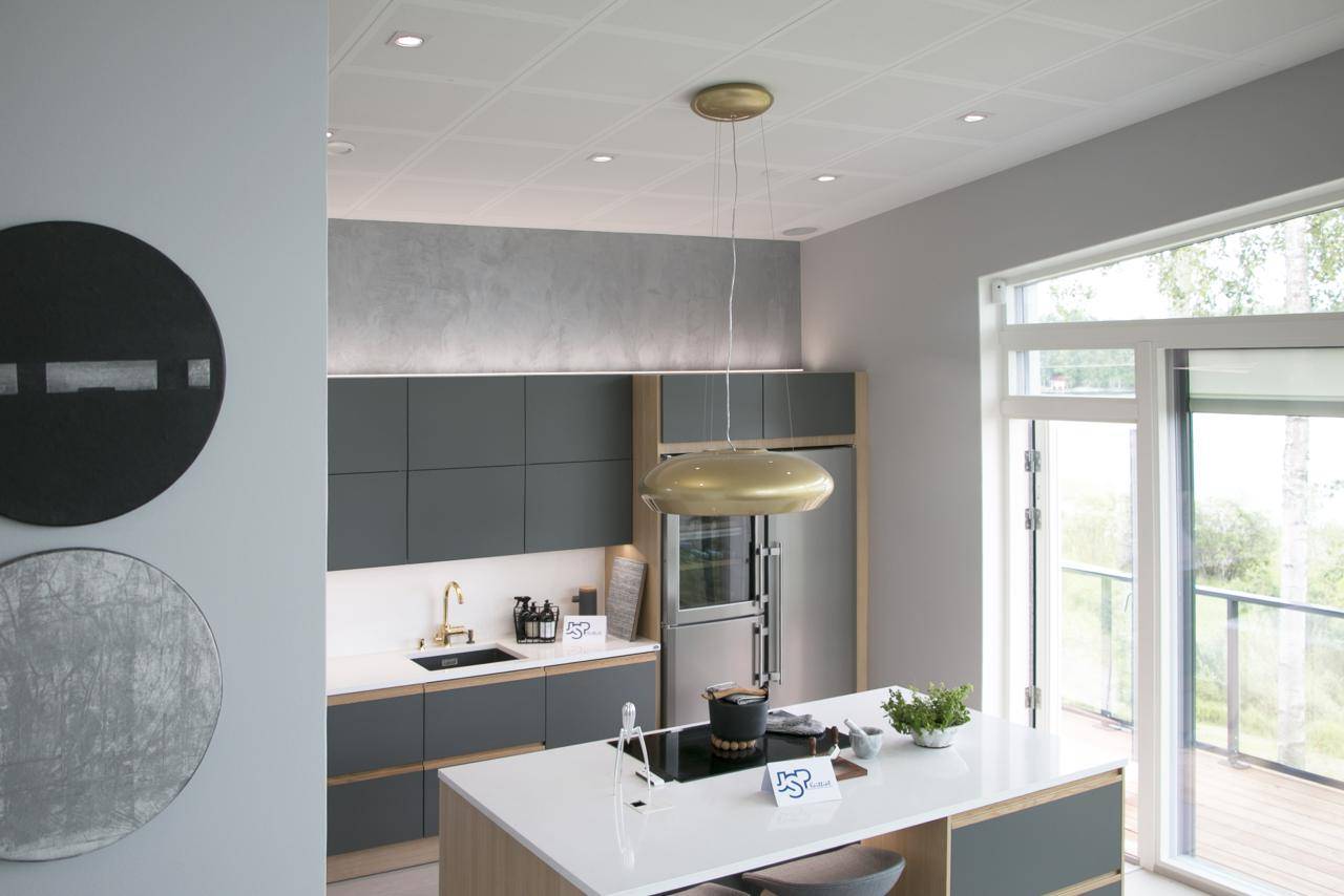 Cucina moderna con armadietti verde scuro, isola bianca, luci a sospensione dorate, elettrodomestici; parete artistica a LED che mette in risalto la luce naturale proveniente dalle grandi finestre.