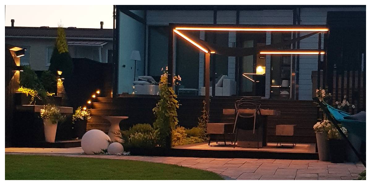 Cortile moderno con pergola e splendida illuminazione a LED. Gradini in legno e suggestive piante in vaso. Situato nel cortile di una casa moderna, l'insieme offre la cornice perfetta per le serate con l'illuminazione LED di alta qualità di LedStore.fi.  