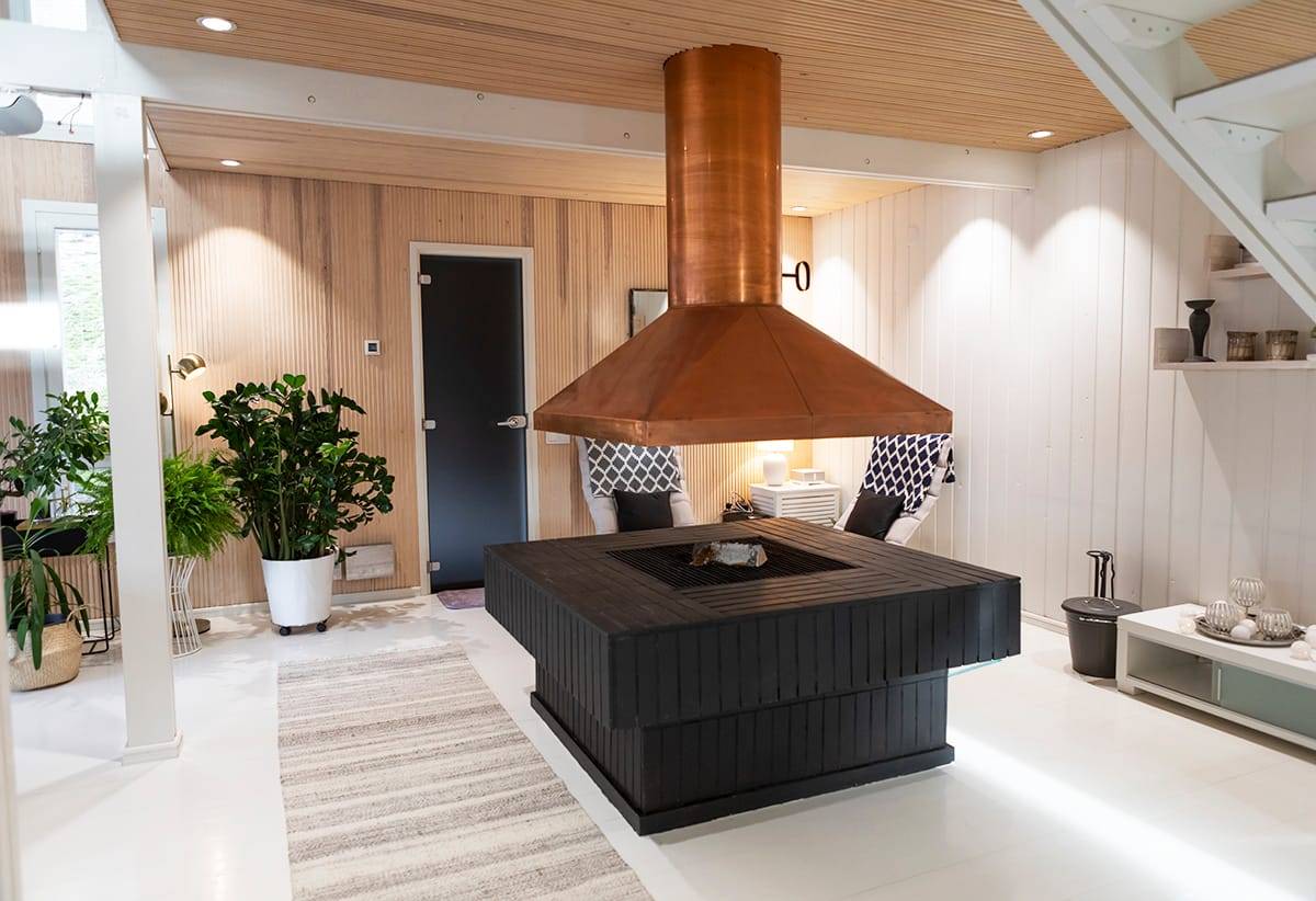 Soggiorno moderno con camino nero e in legno al centro, tubo di rame, illuminazione a LED, sedie imbottite, verde e arredamento elegante.