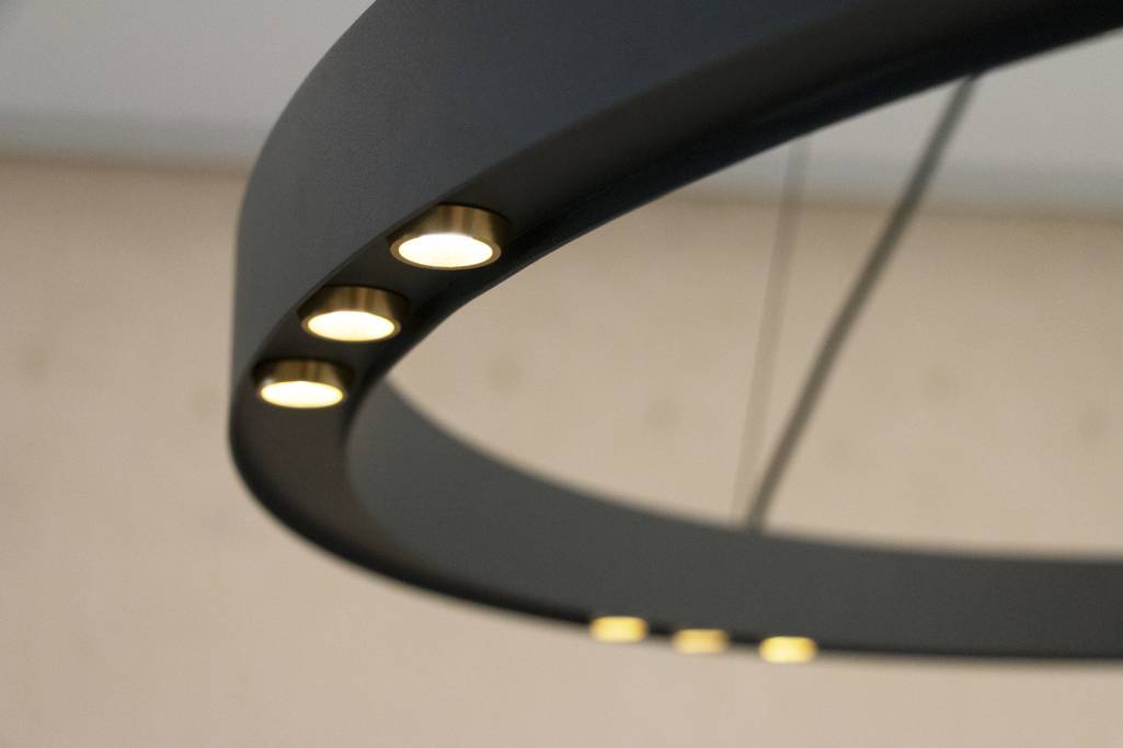 Primo piano di un moderno lampadario rotondo nero opaco con luci LED a incasso che creano una luce morbida su uno sfondo sfocato per un'atmosfera elegante.