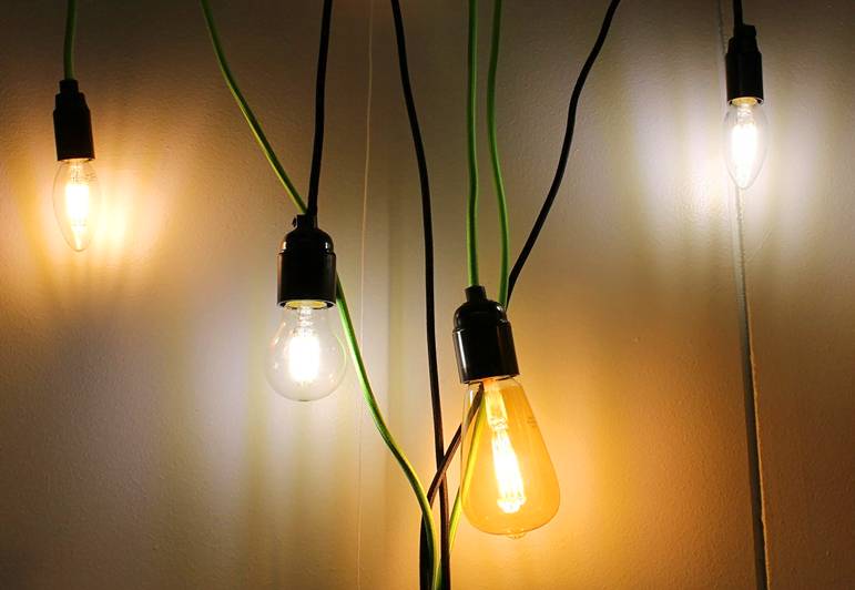 I fili neri e verdi di quattro eleganti lampade LED sono appesi a una parete chiara, per un interno moderno.