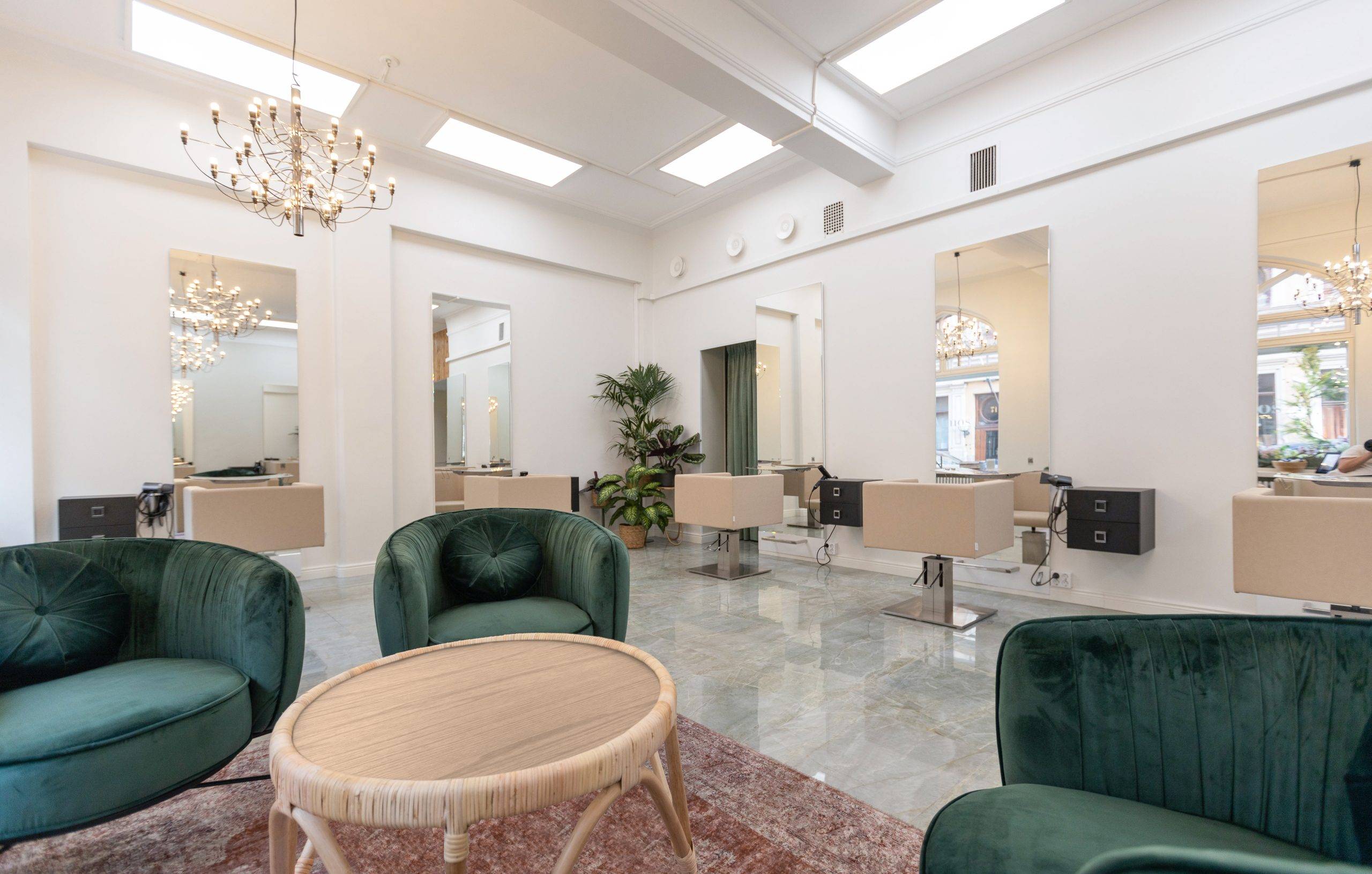 Un salone moderno e luminoso con sedie di velluto verde che circondano un tavolo rotondo con un tappeto rosso. Le postazioni di lavoro del salone, con specchi e sedie beige, sono allineate alle pareti. Sono illuminate da lampadari a LED montati sul soffitto. Le grandi finestre lasciano entrare la luce naturale, mentre il verde arricchisce l'atmosfera dello spazio. In questo tipo di ambiente, le soluzioni di illuminazione a LED di alta qualità di LedStore.fi sono ideali per creare il perfetto equilibrio tra luce e risparmio energetico senza compromettere l'eleganza.