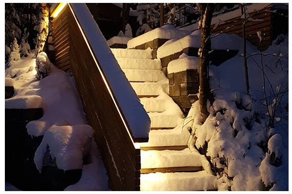 Scale coperte di neve al crepuscolo, con una luce calda che si diffonde dalla ringhiera sulle scale.  
