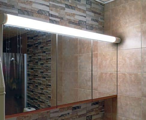 Sopra l'armadio a specchio, una cornice di tubi fluorescenti si illuminava.
